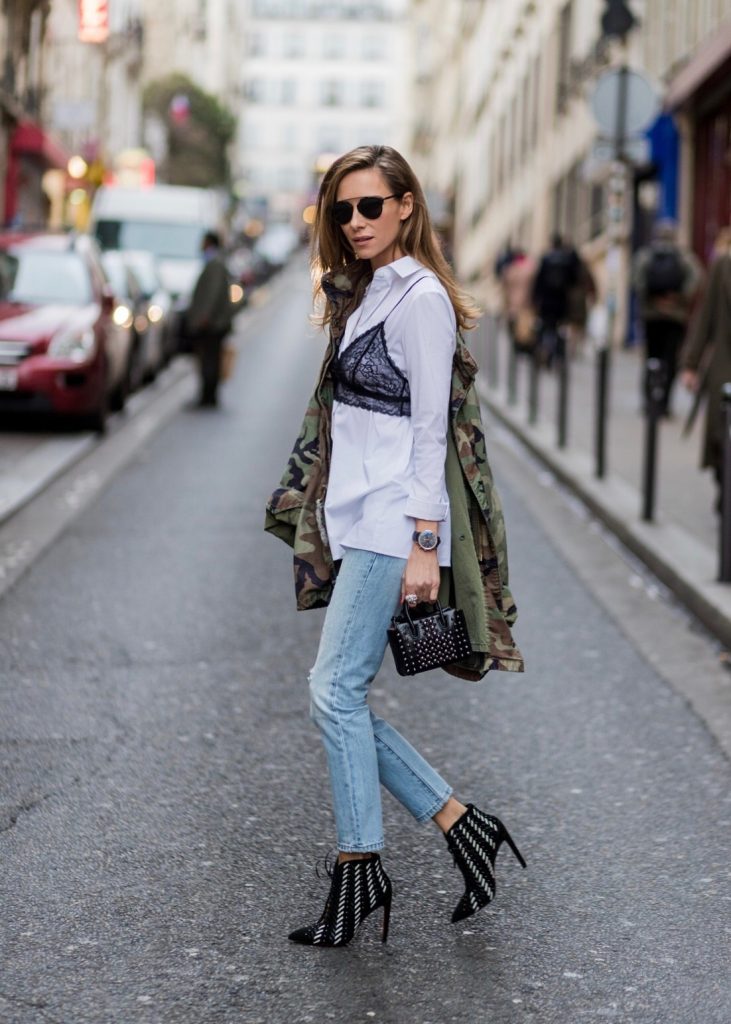 PARIS; FRANCE; Model and Blogger Alexandra Lapp wearing Bra over shirt trend, a light blue Levi's 501 Skinny Jeans with button fly in the classic five-pocket design, signature Levi's tab and arch are stitches on back pockets, white blouse from Acne Studios, Bust Candy Bra Top by FARINA for NA-KD in black features adjustable satin shoulder straps, Mills pearl studs tote bag from MCM in black with hand-applied faux pearls, black and white Santoni ankle boots in suede, original vintage camouflage, army jacket, ring from Cartier on March 4, 2017 in Paris, France.