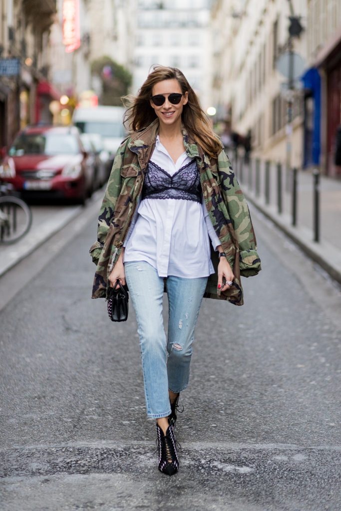 PARIS; FRANCE; Model and Blogger Alexandra Lapp wearing Bra over shirt trend, a light blue Levi's 501 Skinny Jeans with button fly in the classic five-pocket design, signature Levi's tab and arch are stitches on back pockets, white blouse from Acne Studios, Bust Candy Bra Top by FARINA for NA-KD in black features adjustable satin shoulder straps, Mills pearl studs tote bag from MCM in black with hand-applied faux pearls, black and white Santoni ankle boots in suede, original vintage camouflage, army jacket, ring from Cartier on March 4, 2017 in Paris, France.