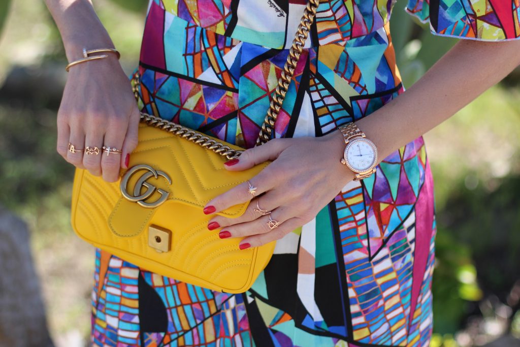 Malibu, Los Angeles; Model and fashion blogger Alexandra Lapp wearing a colorful dress by La Martina, the Polo brand, sandals from Saint Laurent in black with golden rock studs, red lipstick from MAC, a yellow Gucci GG Marmont bag, IWC Da Vinci Automatic 36 watch in 18-carat red gold with diamonds and jewelry from AYS (Art Youth Society) in Malibu on April 17, 2017 in Los Angeles, California.