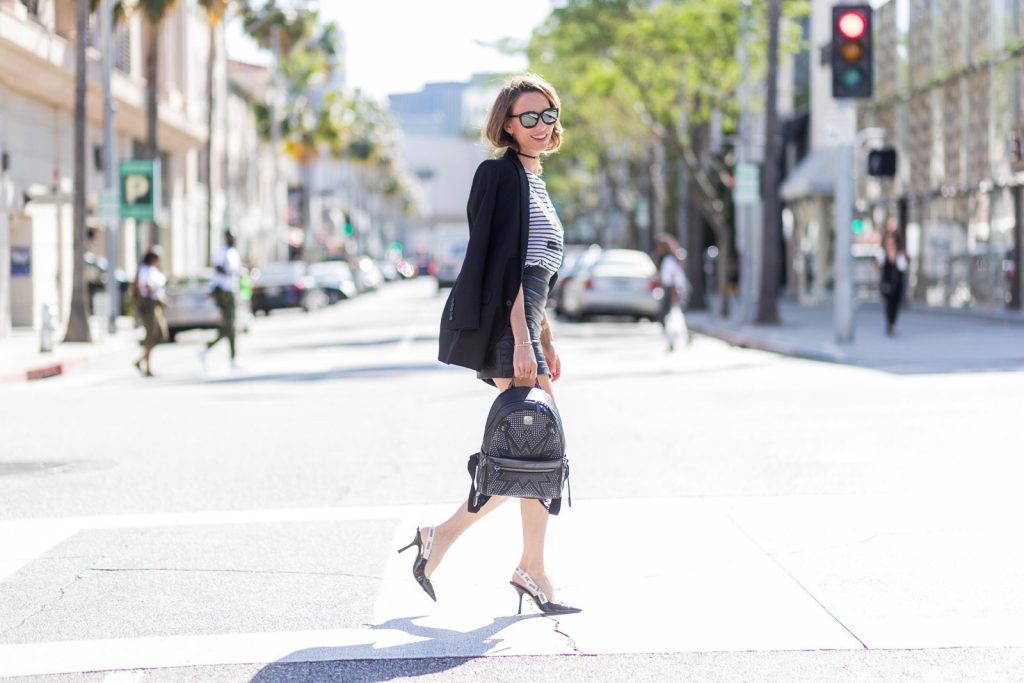 Model and fashion blogger Alexandra Lapp wearing an MCM backpack, high waist mini skirt in black leather with silver buckles from Manokhi Leather, white linen striped zipped top from Karl Lagerfeld, with a leather sunglasses application, Dior Slingback pumps in black patent calfskin leather and J'Adior ribbon with a 10 cm heel, Dior choker around the neck, Diormania sunglasses by Dior, Saint Laurent jacket and the Dual Stark Cyber backpack from MCM with techno-graphic details, made from specially foil-coated black razor cowhide, polished off with applications and studs a plus the front pocket zips off to create a separate crossbody or clutch, IWC Da Vinci Automatic 36 watch in 18-carat red gold with diamonds and jewelry from AYS (Art Youth Society) on April 20, 2017 on Rodeo Drive in Los Angeles, California.