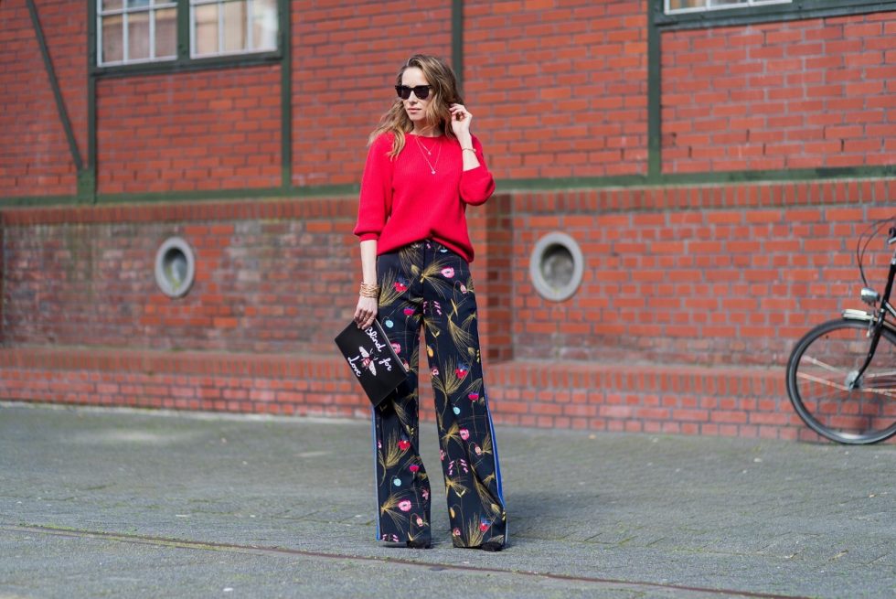 Model and fashion blogger Alexandra Lapp wearing marlene pants, a black and multicoloured floral print trousers from Fendi featuring a high rise, a concealed front fastening, side pockets, applique stripes at the sides, creases and a wide leg, red cashmere knitwear by Valentino, black suede So Kate pumps from Christian Louboutin, gold plated cuff from Gas Bijoux, Celine sunglasses and a black leather ring detail continental purse bag or wallet from Fendi featuring an embossed logo, a press stud fastening, multiple interior card slots, an interior zipped compartment and a gold-tone chain shoulder strap. on March 30, 2017 in Duesseldorf, Germany.