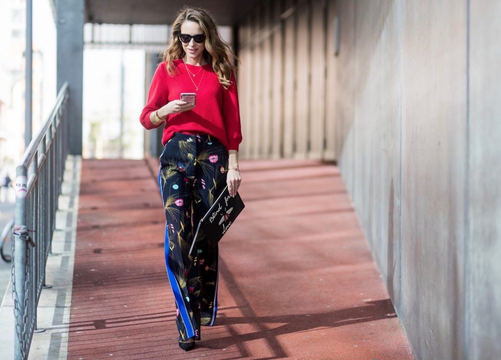 Model and fashion blogger Alexandra Lapp wearing marlene pants, a black and multicoloured floral print trousers from Fendi featuring a high rise, a concealed front fastening, side pockets, applique stripes at the sides, creases and a wide leg, red cashmere knitwear by Valentino, black suede So Kate pumps from Christian Louboutin, gold plated cuff from Gas Bijoux, Celine sunglasses and a black leather ring detail continental purse bag or wallet from Fendi featuring an embossed logo, a press stud fastening, multiple interior card slots, an interior zipped compartment and a gold-tone chain shoulder strap. on March 30, 2017 in Duesseldorf, Germany.