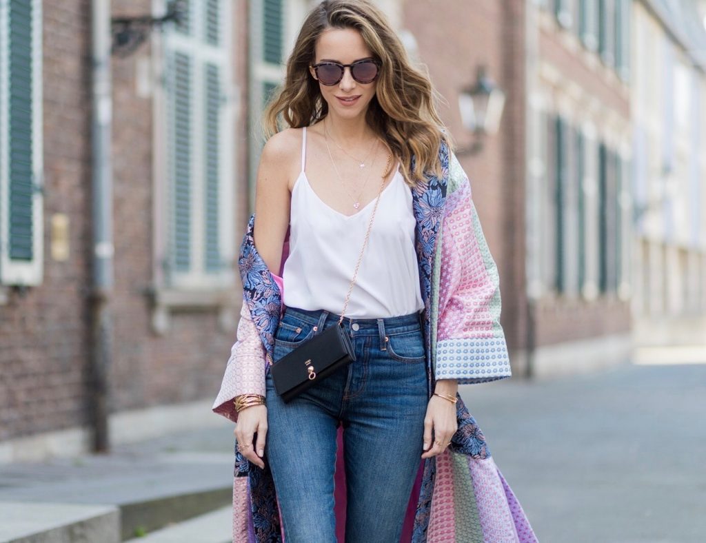 Model and fashion blogger Alexandra Lapp wearing a printed kimono / panel robe from Natasha Zinko, slim fit high waist Jeans from Rag & Bone, Mules by Gucci with open-toe-silhouette in glittery silver grey, white silk tank top from Jadicted, colorful mirrored sunglasses from Les Specs, black leather ring detail continental purse bag from Fendi featuring an embossed logo, a press stud fastening, multiple interior card slots, an interior zipped compartment and a gold-tone chain shoulder strap on March 30, 2017 in Duesseldorf, Germany.