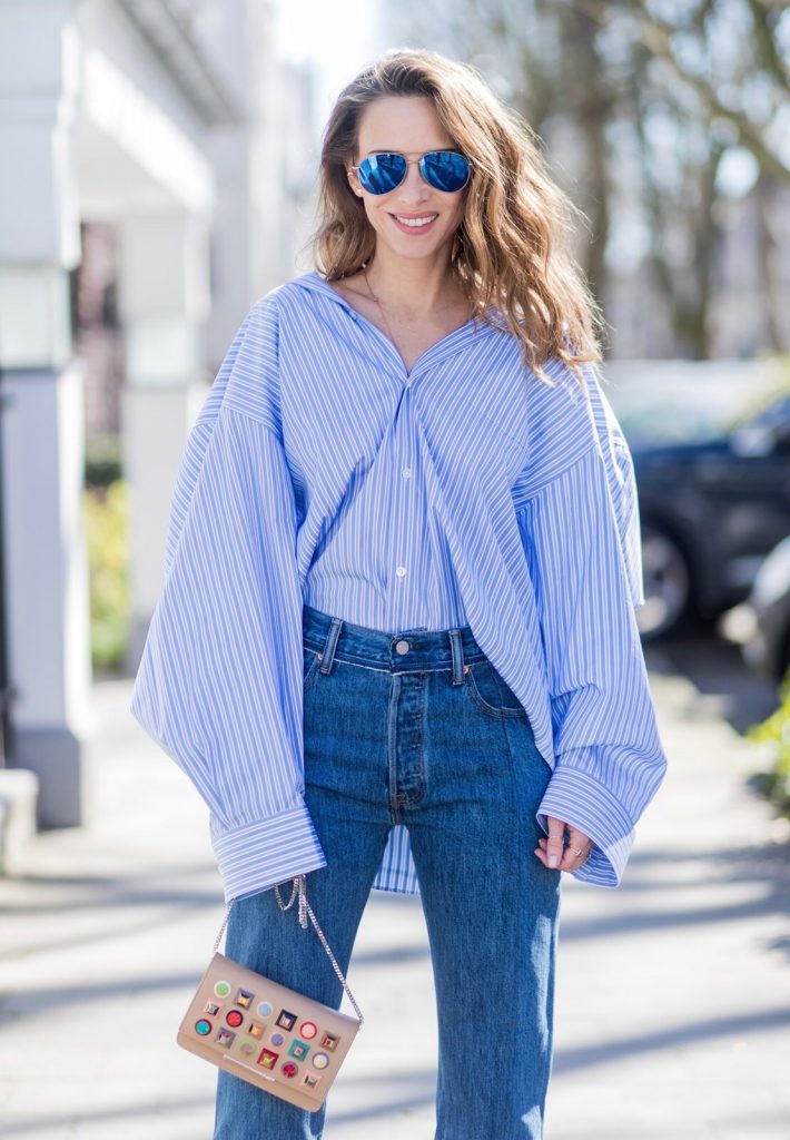 Vetements, Christian Louboutin, Fendi, Illevesta, AYS Model and fashion blogger Alexandra Lapp wearing an oversized navy and white striped cotton shirt, cut for an oversized fit with a point collar and dropped shoulders from Vetements, blue jeans from Vetements in cooperation with Levi`s with cut-out raw hems, blue aviator sunglasses from illevesta, Christian Louboutin pumps in cognac, filigree rose gold jewelry from Art Youth Society and a studded embellished crossbody bag from Fendi featuring a foldover top with magnetic closure, an interior zipped compartment, multiple interior card slots and a silver-tone chain shoulder strap on March 30, 2017 in Duesseldorf, Germany.