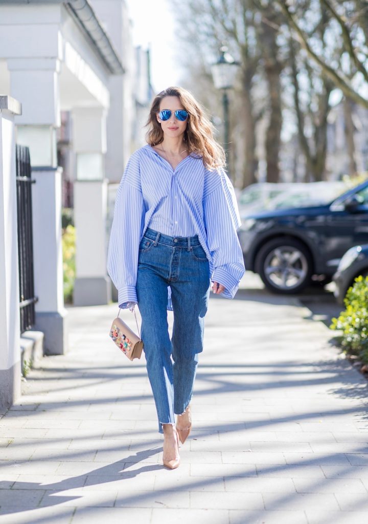 Vetements, Christian Louboutin, Fendi, Illevesta, AYS Model and fashion blogger Alexandra Lapp wearing an oversized navy and white striped cotton shirt, cut for an oversized fit with a point collar and dropped shoulders from Vetements, blue jeans from Vetements in cooperation with Levi`s with cut-out raw hems, blue aviator sunglasses from illevesta, Christian Louboutin pumps in cognac, filigree rose gold jewelry from Art Youth Society and a studded embellished crossbody bag from Fendi featuring a foldover top with magnetic closure, an interior zipped compartment, multiple interior card slots and a silver-tone chain shoulder strap on March 30, 2017 in Duesseldorf, Germany.
