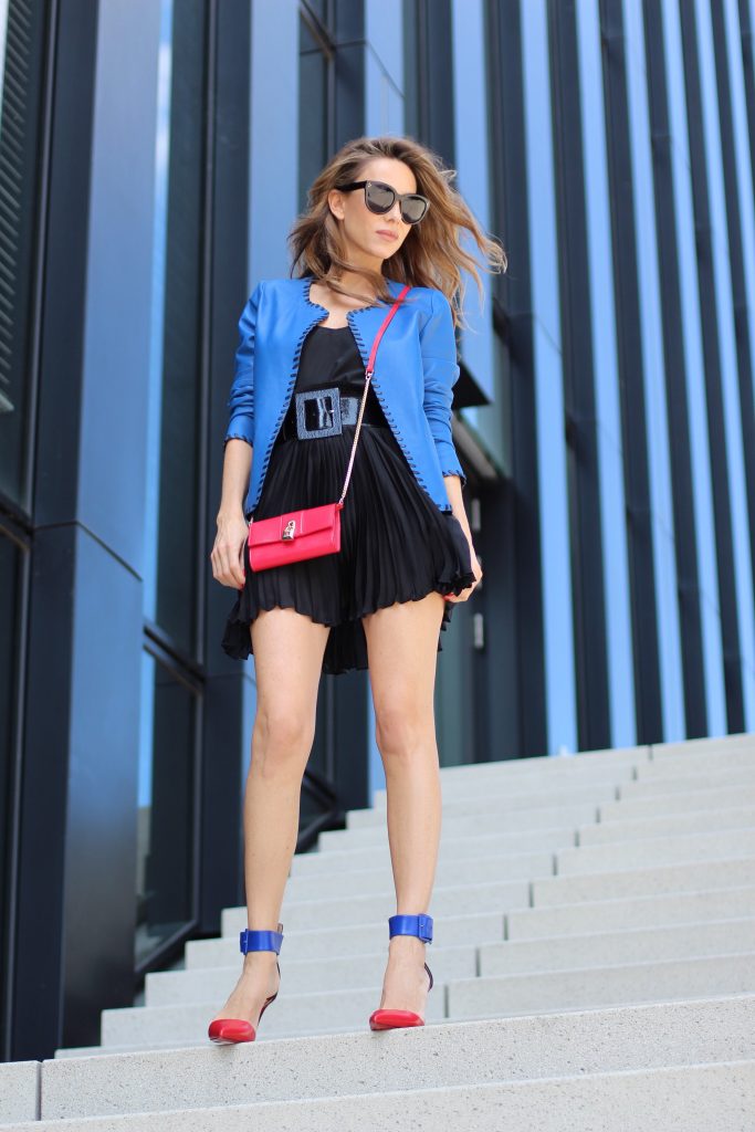 Riani, Dolce & Gabbana, Jadicted, Givenchy, Patrizia Pepe, Céline, Audrey sunglasses, Harler pumps, Christian Louboutin, Model and Blogger Alexandra Lapp wearing a blue leather jacket from Riani, high waist pleated skirt by Givenchy, black silk top from Jadicted, a black lacquer waist belt from Dolce & Gabbana, big cat-eye 'Audrey' sunglasses from Céline, a red crossover purse bag from Patrizia Pepe and 'Harler' 100cm calf multicolor high heels from Christian Louboutin with a red sol, red front, black back and a blue little belt around the ankles, on June 2017 in Duesseldorf.