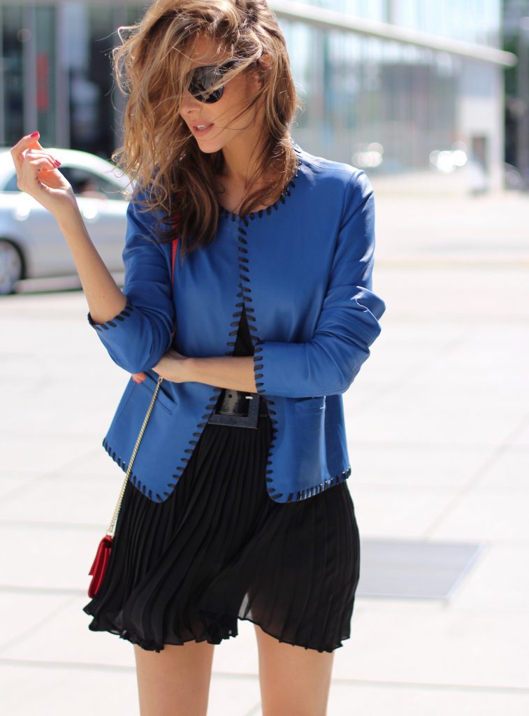 Riani, Dolce & Gabbana, Jadicted, Givenchy, Patrizia Pepe, Céline, Audrey sunglasses, Harler pumps, Christian Louboutin, Model and Blogger Alexandra Lapp wearing a blue leather jacket from Riani, high waist pleated skirt by Givenchy, black silk top from Jadicted, a black lacquer waist belt from Dolce & Gabbana, big cat-eye 'Audrey' sunglasses from Céline, a red crossover purse bag from Patrizia Pepe and 'Harler' 100cm calf multicolor high heels from Christian Louboutin with a red sol, red front, black back and a blue little belt around the ankles, on June 2017 in Duesseldorf.