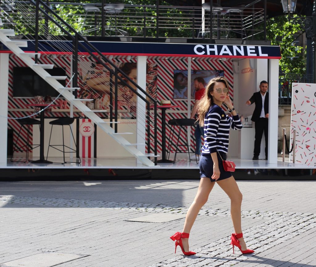 Model and Blogger Alexandra Lapp sitting at Coco Café #cococafe in Duesseldorf, wearing a blue white striped cashmere pullover with gold buttons from Heartbreaker, a dark blue silk shorts by Prada, satin Douce du desert pumps in red with a big silk bow from Christian Louboutin, red crossover purse-bag from Patrizia Pepe and gold cat-eye sunglasses from KARL by Karl Lagerfeld, in Duesseldorf on June, 14th 2017. 