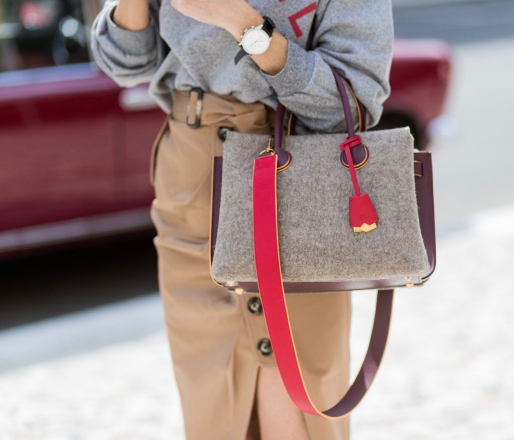 Alexandra Lapp (model, blogger) wearing a vintage sweater from Chanel in grey melange, printed with Chanel red capital letters, a red lipstick and a powder box from Chanel, a midi skirt in a trench silhouette from Self-Portrait, with beige cotton and utilitarian buttons, a belt and a asymmetric cut with a thigh-high slit, red Christian Louboutin pumps in crepe de satin, MCM Milla Spanish leather Tote bag and black Celine Audrey sunglasses during the Mercedes-Benz Fashion Week Berlin Spring/Summer 2018 on July 6, 2017 in Berlin, Germany. (Photo by Christian Vierig)
