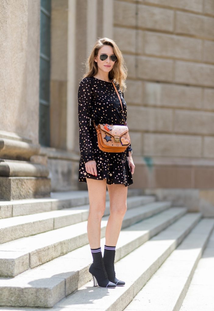 Sock Boots, Fendi, Valentino R.E.D., MCM, Ray Ban, Berlin, MBFWB, MBFW Alexandra Lapp (model, blogger) wearing Fendis SS 17 collection sock boots with a grey knit upper, with a high sculptural heel, a black silk chiffon mini dress with gilded stars from RED Valentino with a tie at the neck and a ruffle through the hem, a MCM Patricia Shoulder Bag crafted in in Visetos-print coated canvas and topped with crystalized appliqués, including the Punk Rabbit, accented with mink fur, studwork and edge painting and a laurel-engraved case latch closure and Ray Ban aviator sunglasses in gold during the Mercedes-Benz Fashion Week Berlin Spring/Summer 2018 on July 6, 2017 in Berlin, Germany.