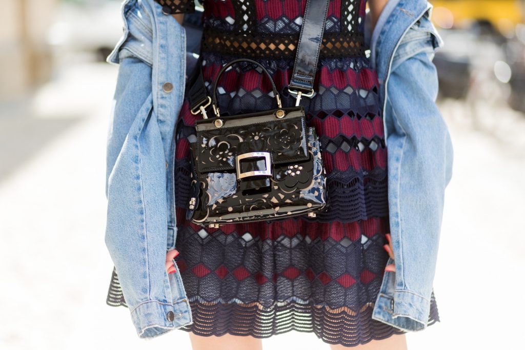 Alexandra Lapp (model, blogger) wearing a mini lace dress in navy blue and heady red from Self-Portrait, a Roger Viv mini bag crafted in suede with waterjet cut Guipure detailing, flap, clasp fastening, metal buckle and details, handle and leather removable strap in trapezium shape and ankle boots from Roger Vivier in black patent leather, denim jacket by SET, brown sunglasses with pearls by Chanel and Fendi during the Mercedes-Benz Fashion Week Berlin Spring/Summer 2018 on July 6, 2017 in Berlin, Germany.