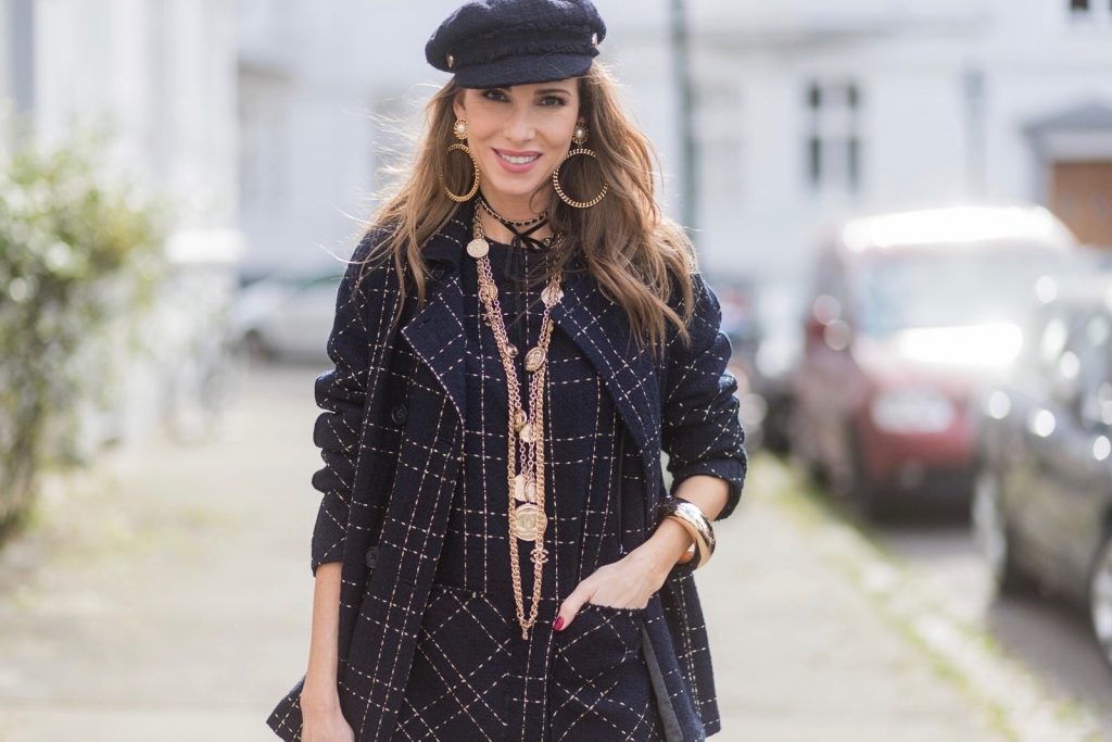 Model and fashion blogger Alexandra Lapp wearing a look inspired by Chanel, a tweed dress and coat from Steffen Schraut, Balmain x HM sandals, Strak backpack by MCM, Chanel tweed cap, golden Chanel chains in form from Chanel coins, Chanel chocker and golden bracelet from Schubart Goldschmiede and golden vintage earrings with a peals by Chanel on August 5, 2017 in Duesseldorf, Germany.
