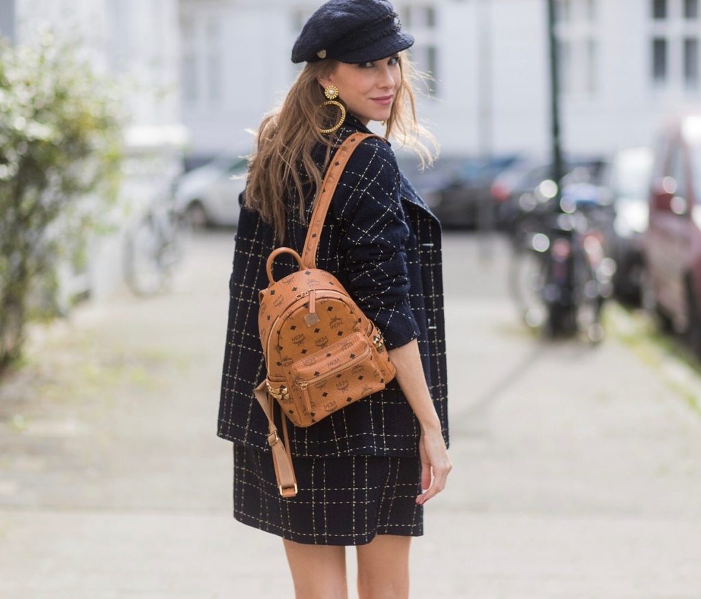 Model and fashion blogger Alexandra Lapp wearing a look inspired by Chanel, a tweed dress and coat from Steffen Schraut, Balmain x HM sandals, Strak backpack by MCM, Chanel tweed cap, golden Chanel chains in form from Chanel coins, Chanel chocker and golden bracelet from Schubart Goldschmiede and golden vintage earrings with a peals by Chanel on August 5, 2017 in Duesseldorf, Germany.