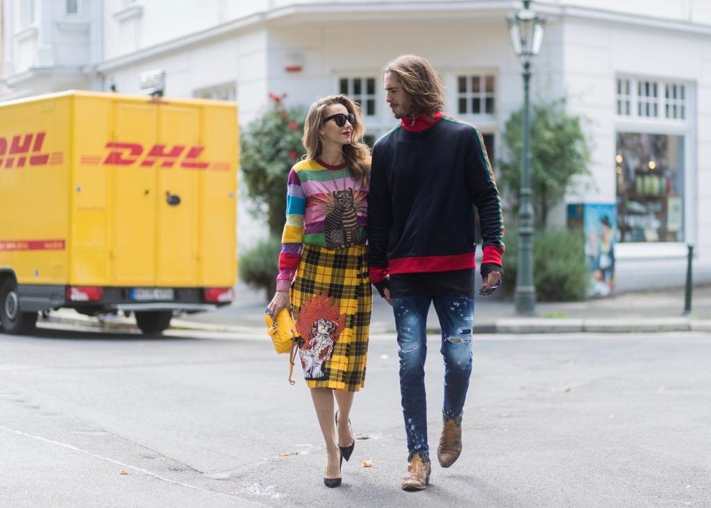 Gucci, Celine, Schubart, Christian Louboutin, couple look, Couple look a like holding hands in front of DHL van - Model and Blogger Alexandra Lapp wearing a Gucci total look, a yellow and red pleated tartan skirt embroidered with a spaniel dog and belt buckle closure, colorful striped sweater with lace and merino with embroidered cat applique all Gucci, black Christian Louboutin So Kate pumps, GG Marmont Gucci bag in yellow, Audrey sunglasses from Celine and Model and Blogger Thomas Stuch wearing classic Kenny Twist Jean from Dsquared, black T-Shirt Thom Krom, Gucci track suit top, Stallion Cowboy Boots on August 4, 2017 in Duesseldorf, Germany.