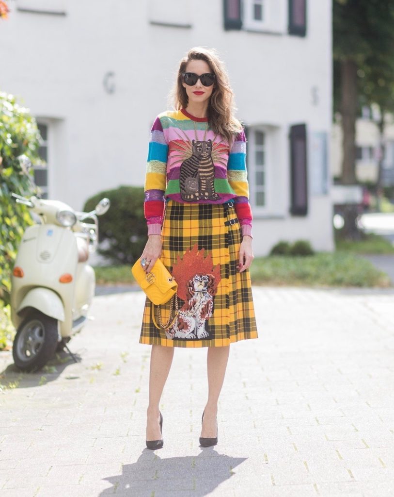 Gucci, Celine, Schubart, Christian Louboutin, Model and Blogger Alexandra Lapp wearing a Gucci total look, yellow and red pleated tartan skirt embroidered with a spaniel dog and belt buckle closure, colorful striped sweater with lace and merino with embroidered cat applique all Gucci, black Christian Louboutin So Kate pumps, GG Marmont Gucci bag in yellow, Audrey sunglasses from Celine on August 4, 2017 in Duesseldorf, Germany.