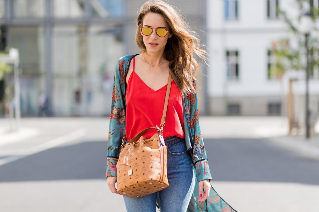 Model and fashion blogger Alexandra Lapp wearing a wrap dress in Kimono style from Zara, silk tank top from Jadicted, petite bucket bag from MCM, Levis Wedgie Icon Fit jeans in slim fit, So Kate pumps in cognac by Christian Louboutin and gold mirrored aviator sunglasses by Thom Browne during the Mercedes-Benz Fashion Week Berlin Spring/Summer 2018 on July 8, 2017 in Berlin, Germany.