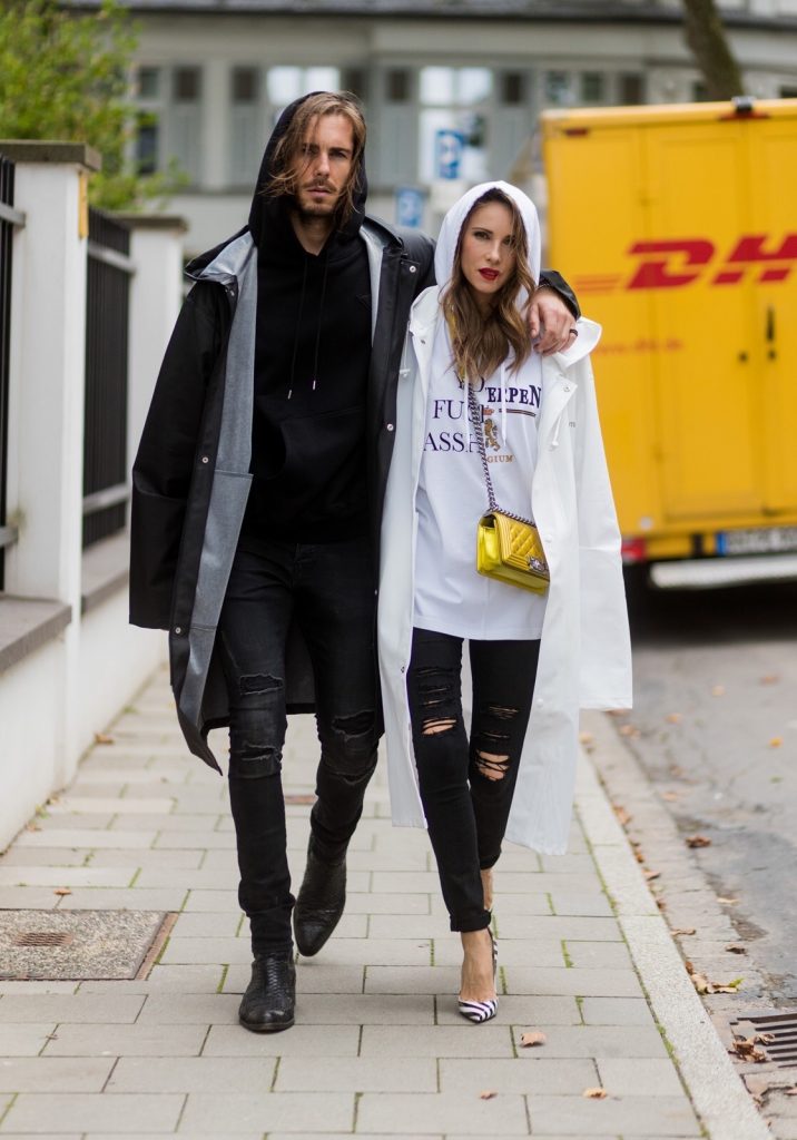 Couple look a like holding arms in front of a DHL van - Model and Blogger Alexandra Lapp wearing oversized Vetements raincoat with a hood in white, Vetements hoodie in white, destroyed Adriano Goldschmied high waist denim in black, black and white So Kate pumps with a yellow heel, yellow golden lacquer Boy bag from Chanel and a big golden ring with baguette diamonds from Schubart Goldschmiede and Model and Blogger Thomas Stuch wearing black oversized raincoat with a hood in black from Vetements, Stella McCartney hoodie in black, Dsquared slim fit denim, Ghost cowboy boots on August 4, 2017 in Duesseldorf, Germany.