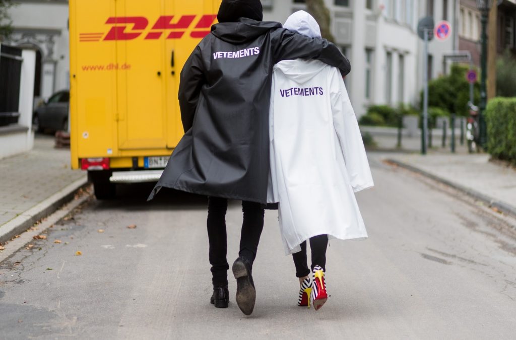 Couple look a like holding arms in front of a DHL van - Model and Blogger Alexandra Lapp wearing oversized Vetements raincoat with a hood in white, Vetements hoodie in white, destroyed Adriano Goldschmied high waist denim in black, black and white So Kate pumps with a yellow heel, yellow golden lacquer Boy bag from Chanel and a big golden ring with baguette diamonds from Schubart Goldschmiede and Model and Blogger Thomas Stuch wearing black oversized raincoat with a hood in black from Vetements, Stella McCartney hoodie in black, Dsquared slim fit denim, Ghost cowboy boots on August 4, 2017 in Duesseldorf, Germany.