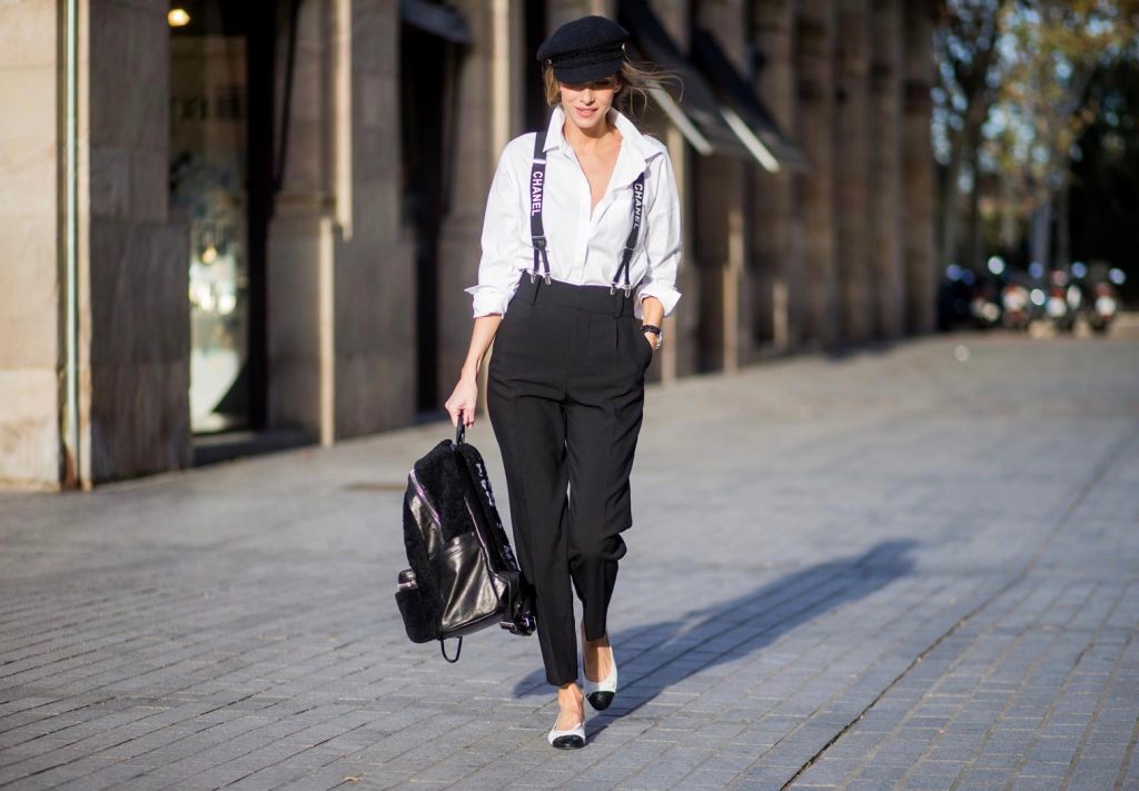 Alexandra Lapp wearing black and white vintage Chanel suspenders with Chanel logo in black and white, a white oversized shirt from Steffen Schraut, black high waist pants from Zara, XL backpack in lambskin with black and white MCM logo and Chanel baker boy cap in black tweed and ballerinas in white with black tip and logo from Chanel on November 27, 2017 in Barcelona, Spain.