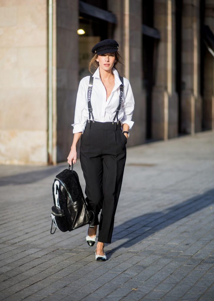Alexandra Lapp wearing black and white vintage Chanel suspenders with Chanel logo in black and white, a white oversized shirt from Steffen Schraut, black high waist pants from Zara, XL backpack in lambskin with black and white MCM logo and Chanel baker boy cap in black tweed and ballerinas in white with black tip and logo from Chanel on November 27, 2017 in Barcelona, Spain.