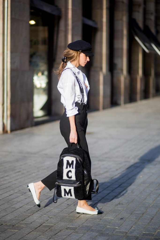 Alexandra Lapp wearing black and white vintage Chanel suspenders with Chanel logo in black and white, a white oversized shirt from Steffen Schraut, black high waist pants from Zara, XL backpack in lambskin with black and white MCM logo and Chanel baker boy cap in black tweed and ballerinas in white with black tip and logo from Chanel on November 27, 2017 in Barcelona, Spain.