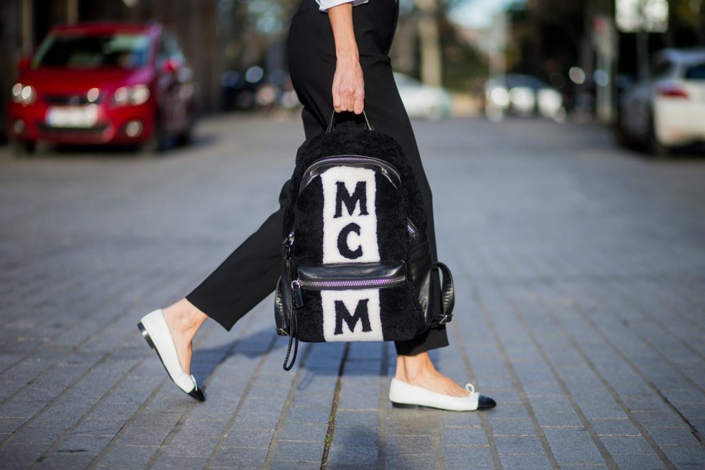Alexandra Lapp wearing black and white vintage Chanel suspenders with Chanel logo in black and white, a white oversized shirt from Steffen Schraut, black high waist pants from Zara, XL backpack in lambskin with black and white MCM logo and Chanel baker boy cap in black tweed and ballerinas in white with black tip and logo from Chanel on November 27, 2017 in Barcelona, Spain.