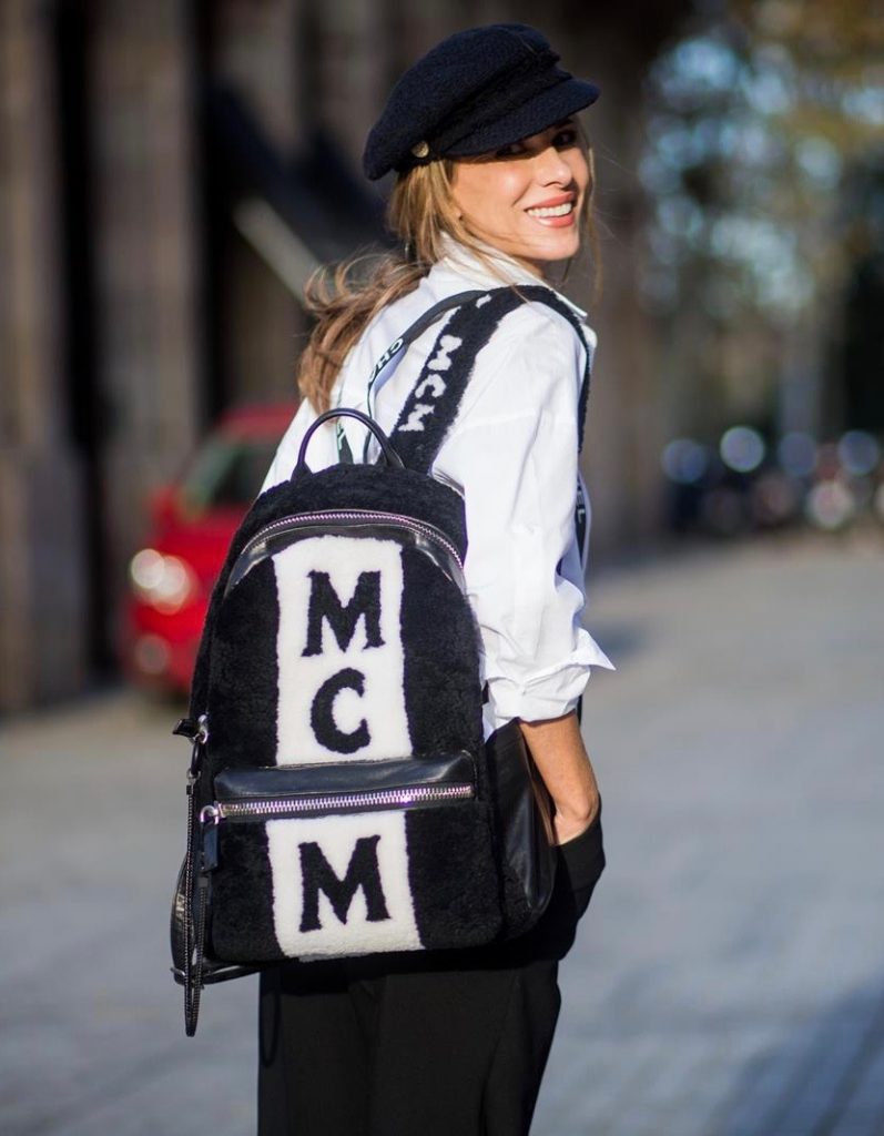 Alexandra Lapp wearing black and white vintage Chanel suspenders with Chanel logo in black and white, a white oversized shirt from Steffen Schraut, black high waist pants from Zara, XL backpack in lambskin with black and white MCM logo and Chanel baker boy cap in black tweed and ballerinas in white with black tip and logo from Chanel on November 27, 2017 in Barcelona, Spain.