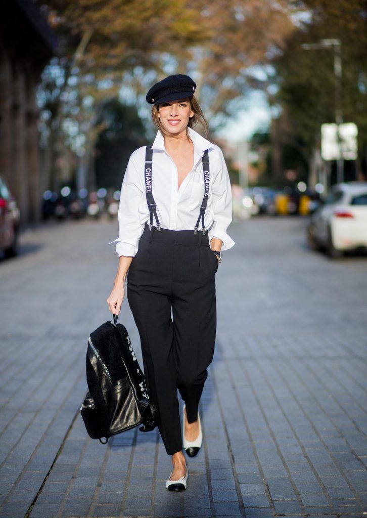 Alexandra Lapp wearing black and white vintage Chanel suspenders with Chanel logo in black and white, a white oversized shirt from Steffen Schraut, black high waist pants from Zara, XL backpack in lambskin with black and white MCM logo and Chanel baker boy cap in black tweed and ballerinas in white with black tip and logo from Chanel on November 27, 2017 in Barcelona, Spain.