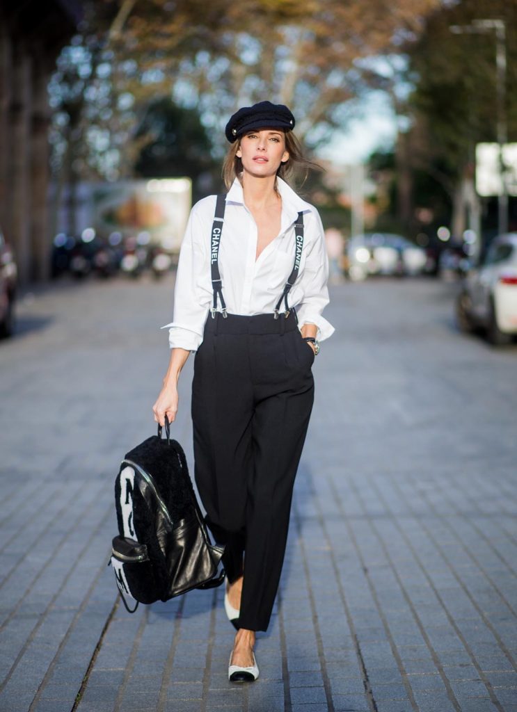 Alexandra Lapp wearing black and white vintage Chanel suspenders with Chanel logo in black and white, a white oversized shirt from Steffen Schraut, black high waist pants from Zara, XL backpack in lambskin with black and white MCM logo and Chanel baker boy cap in black tweed and ballerinas in white with black tip and logo from Chanel on November 27, 2017 in Barcelona, Spain.