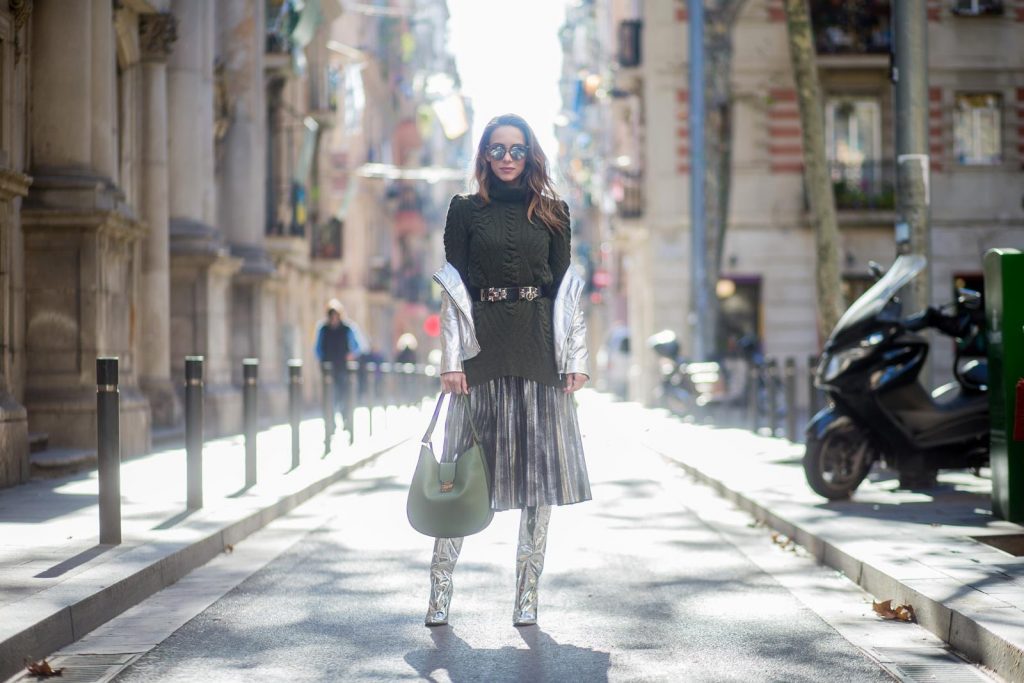Alexandra Lapp wearing metallic look, a pleated skirt in a washed out silver metallic and black style, long knitted dark green Celine turtle neck pullover with cable stitch, black waist belt from Hermes with heavy silver buckle and silver stud details, short cut silver leather jacket with zippers from Set Fashion, silver metallic boots from H&M, large green Patricia Hobo bag from MCM and sunglasses from Le Specs on November 28, 2017 in Barcelona, Spain.