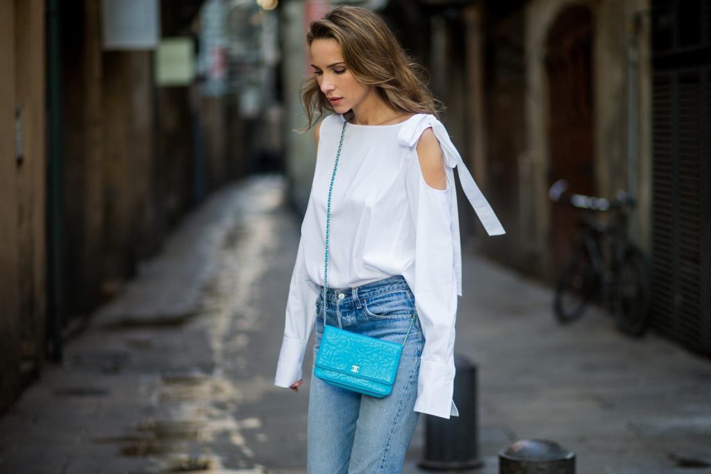 Street Style In Barcelona BARCELONA, SPAIN - NOVEMBER 29: Alexandra Lapp wearing white off-shoulder blouse and light blue lace coat with flowers from Steffen Schraut, silver mirrored sunglasses from Le Specs, multicolored Sophia Webster sandals heels, vintage Levis from ReDone and Chanel purse bag with a long golden strap and Chanel sign in front on November 29, 2017 in Barcelona, Spain.