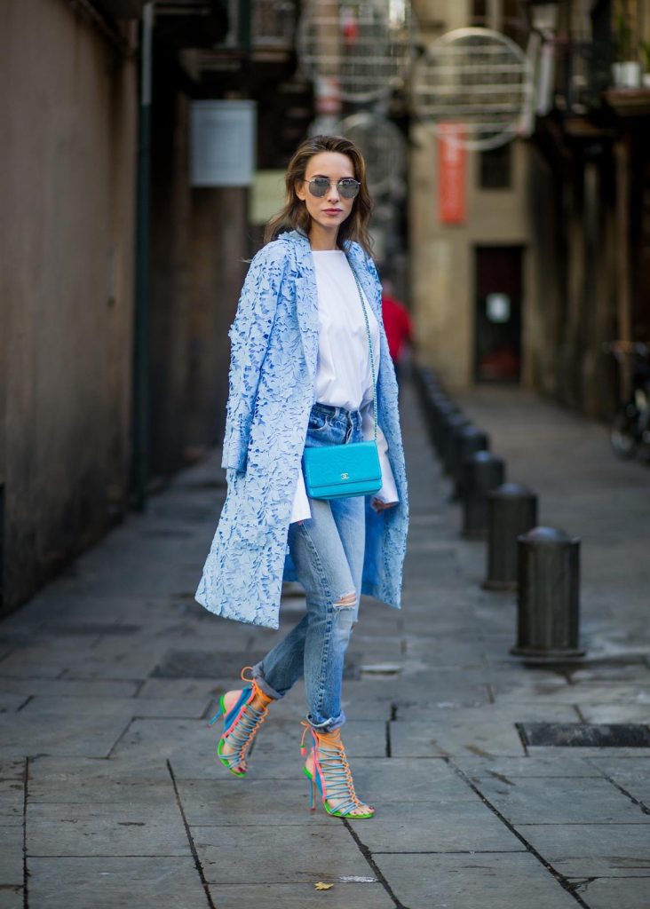Street Style In Barcelona BARCELONA, SPAIN - NOVEMBER 29: Alexandra Lapp wearing white off-shoulder blouse and light blue lace coat with flowers from Steffen Schraut, silver mirrored sunglasses from Le Specs, multicolored Sophia Webster sandals heels, vintage Levis from ReDone and Chanel purse bag with a long golden strap and Chanel sign in front on November 29, 2017 in Barcelona, Spain.
