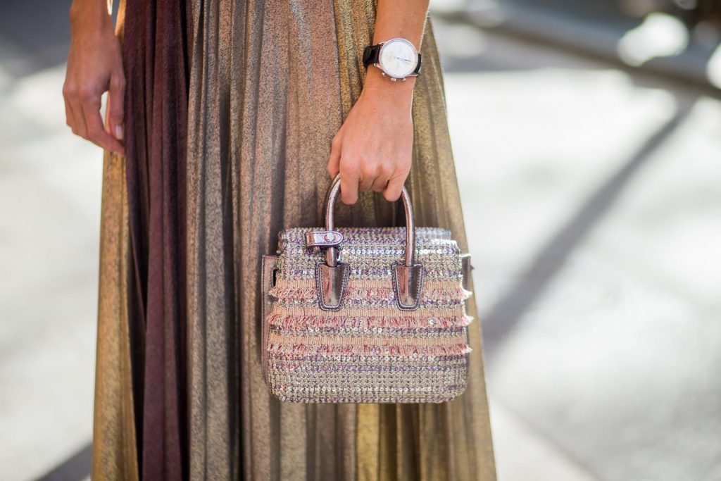 Alexandra Lapp wearing a long pleated metallic skirt with changing gold and red colors, grey cashmere cardigan with pearl buttons and blue and white rims, white and black lacquer waist belt from Balmain with gold buckle and details, Milla handbag in crystal tweed from MCM with metallic yarn and czech crystals, white and green Adidas Stan Smith sneakers and black Celine sunglasses on November 27, 2017 in Barcelona, Spain.