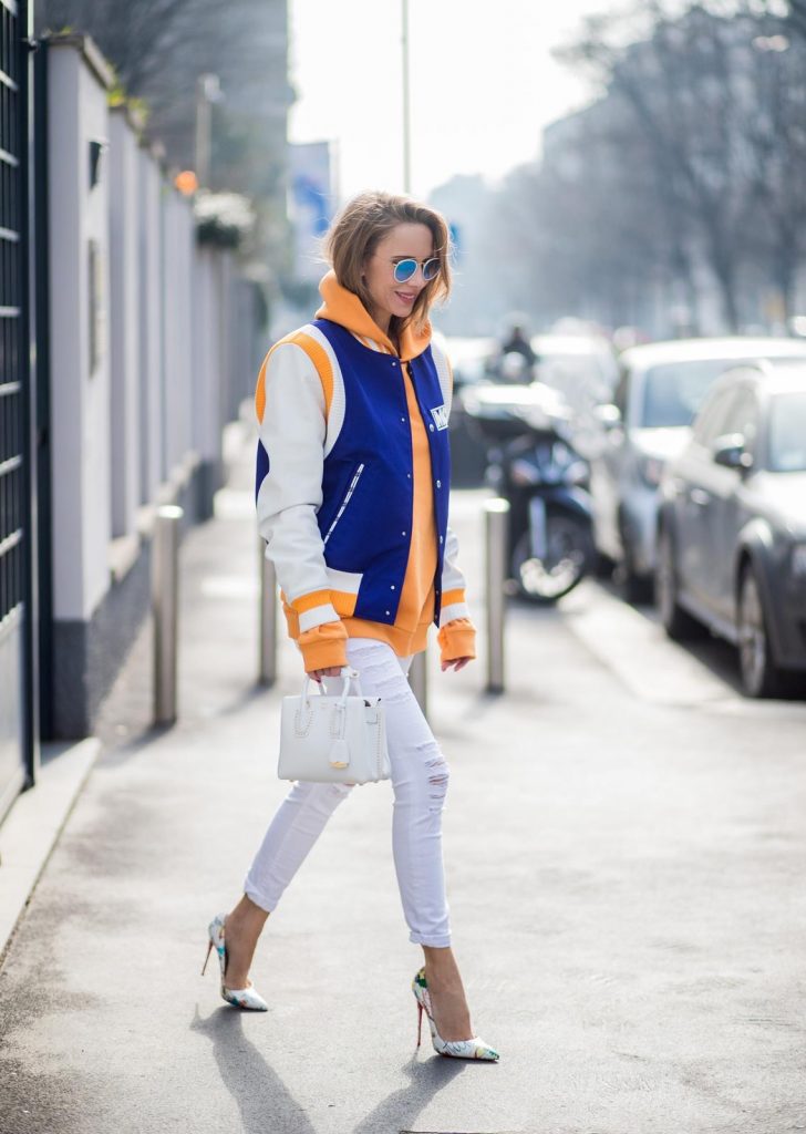 MILAN, ITALY - FEBRUARY 21: Alexandra Lapp wearing college style, a college jacket in blue, white and orange from MCM, an orange hoodie from glam-o-meter, white destroyed jeans from Frame a white Milla handbag from MCM, white pumps from Christian Louboutin and Ray-Ban sunglasses seen during Milan Fashion Week Fall/Winter 2018/19 on February 21, 2018 in Milan, Italy.