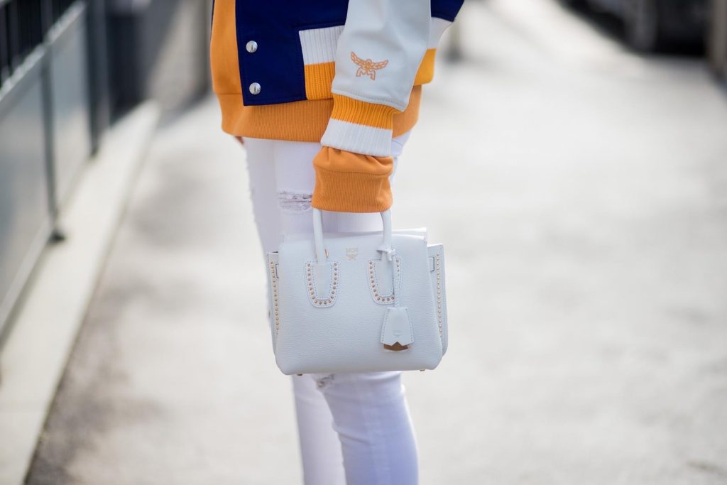 MILAN, ITALY - FEBRUARY 21: Alexandra Lapp wearing college style, a college jacket in blue, white and orange from MCM, an orange hoodie from glam-o-meter, white destroyed jeans from Frame a white Milla handbag from MCM, white pumps from Christian Louboutin and Ray-Ban sunglasses seen during Milan Fashion Week Fall/Winter 2018/19 on February 21, 2018 in Milan, Italy.