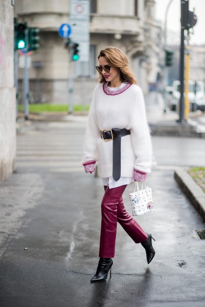 Dorothee Schumacher, MCM, Gianvito Rossi, Maison Mävada Alexandra Lapp wearing flared leather pants in bordeaux by Dorothee Schumacher, an off-white cotton pullover with a bordeaux colored neckline and a long white shirt with a waist line by Dorothee Schumacher, a long black leather belt with a big buckle by Dorothee Schumacher, black leather ankle boots by Gianvito Rossi, cat-eye sunglasses in black with a golden rim by Maison Masada and Anya mini shopper in victory patch from MCM seen during Milan Fashion Week Fall/Winter 2018/19 on February 24, 2018 in Milan, Italy.