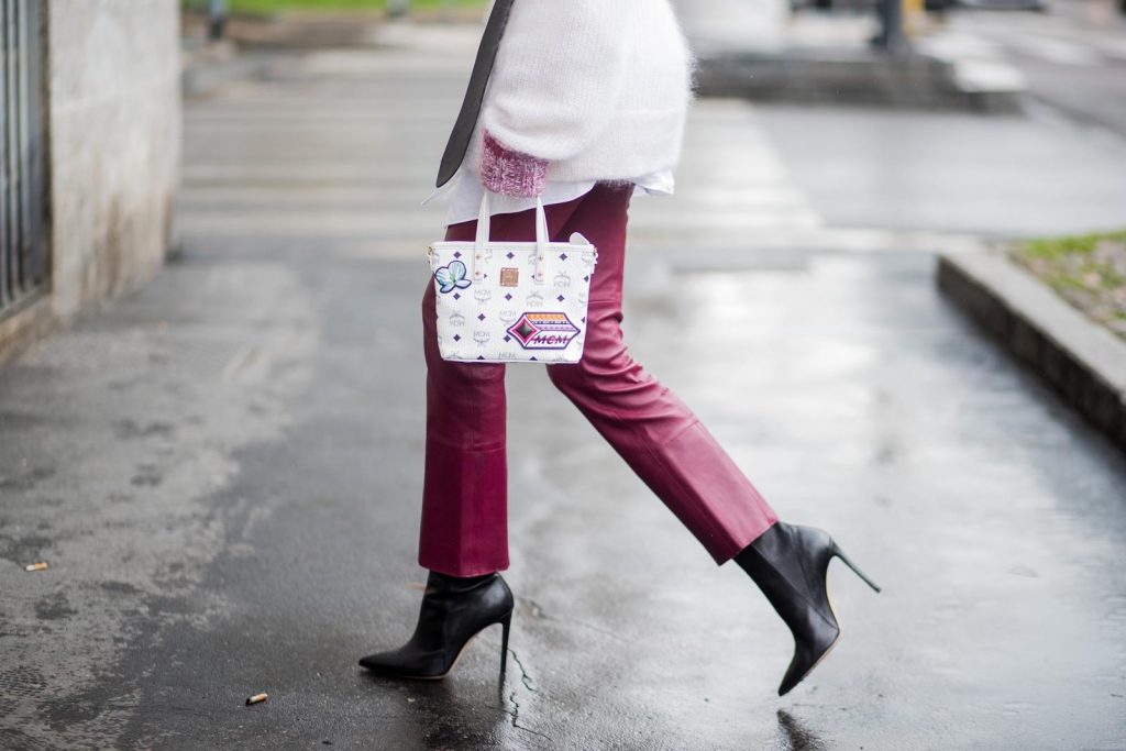 Dorothee Schumacher, MCM, Gianvito Rossi, Maison Mävada Alexandra Lapp wearing flared leather pants in bordeaux by Dorothee Schumacher, an off-white cotton pullover with a bordeaux colored neckline and a long white shirt with a waist line by Dorothee Schumacher, a long black leather belt with a big buckle by Dorothee Schumacher, black leather ankle boots by Gianvito Rossi, cat-eye sunglasses in black with a golden rim by Maison Masada and Anya mini shopper in victory patch from MCM seen during Milan Fashion Week Fall/Winter 2018/19 on February 24, 2018 in Milan, Italy.