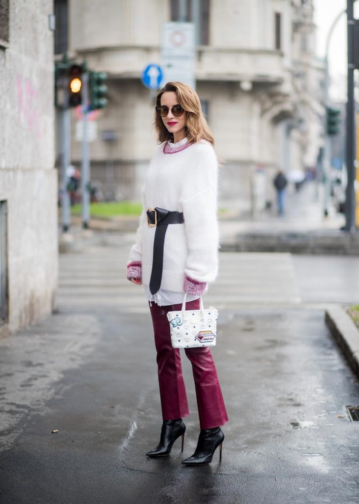 Dorothee Schumacher, MCM, Gianvito Rossi, Maison Mävada Alexandra Lapp wearing flared leather pants in bordeaux by Dorothee Schumacher, an off-white cotton pullover with a bordeaux colored neckline and a long white shirt with a waist line by Dorothee Schumacher, a long black leather belt with a big buckle by Dorothee Schumacher, black leather ankle boots by Gianvito Rossi, cat-eye sunglasses in black with a golden rim by Maison Masada and Anya mini shopper in victory patch from MCM seen during Milan Fashion Week Fall/Winter 2018/19 on February 24, 2018 in Milan, Italy.