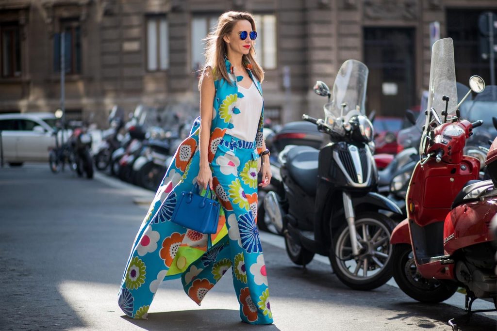 Alexandra Lapp in Seventies Style wearing flower power silk jacquard pants in multicolor with a long leg by Talbot Runhof with matching long vest made of flower power jacquard in multicolor, white silk shirt from Jadicted, blue neo Milla tote bag, Pigalle Follies pumps by Christian Louboutin and blue round sunglasses from Mykita seen during Milan Fashion Week Fall/Winter 2018/19 on February 21, 2018 in Milan, Italy.