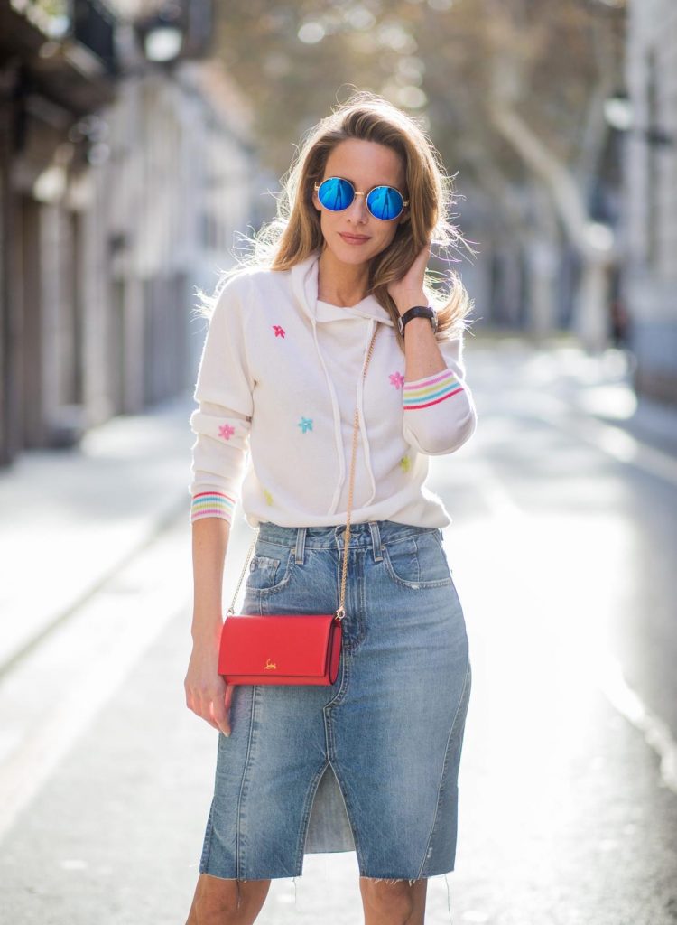 BARCELONA, SPAIN - NOVEMBER 27: Alexandra Lapp wearing a white cashmere hoodie with colored flower applications from Heartbreaker, high rise jeans skirt with slit Adriano Goldschmied, red little purse bag with gold chain from Christian Louboutin, peep-toe pump Christian Louboutin with a long satin bow, sunglasses with round blue shades from Mykita on November 27, 2017 in Barcelona, Spain. 