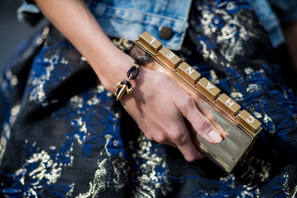 Alexandra Lapp wearing a Marchesa Notte dress with tiered corded lace and brocade in a mix of black, midnight-blue and gold by Marchesa Notte, blue trucker denim jacket by Levis, a gold buckle belt by Dorothee Schumacher, black Nosy t-bar Christian Louboutin sandals with a studded strap, handmade bracelet with rosegold fleur de lis lock by Coerlys and a vintage Chanel clutch in gold on May 3, 2018 in Duesseldorf, Germany.