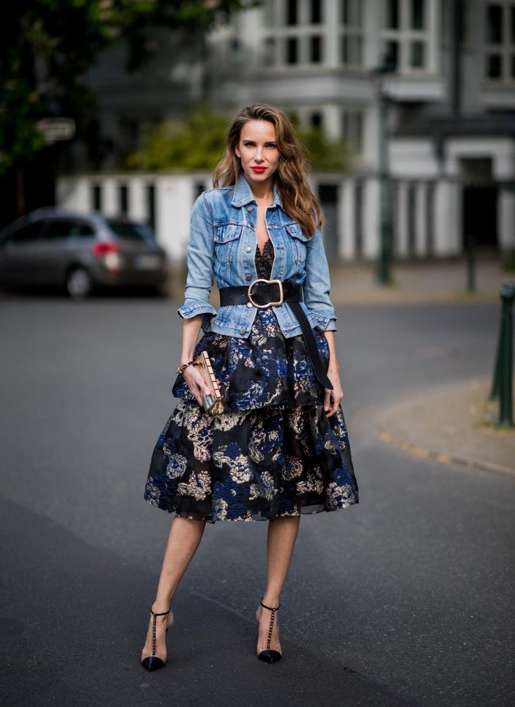 Alexandra Lapp wearing a Marchesa Notte dress with tiered corded lace and brocade in a mix of black, midnight-blue and gold by Marchesa Notte, blue trucker denim jacket by Levis, a gold buckle belt by Dorothee Schumacher, black Nosy t-bar Christian Louboutin sandals with a studded strap, handmade bracelet with rosegold fleur de lis lock by Coerlys and a vintage Chanel clutch in gold on May 3, 2018 in Duesseldorf, Germany.