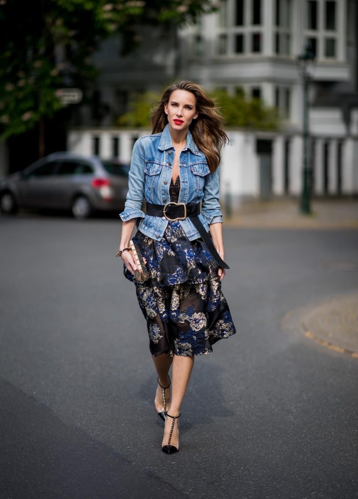 Alexandra Lapp wearing a Marchesa Notte dress with tiered corded lace and brocade in a mix of black, midnight-blue and gold by Marchesa Notte, blue trucker denim jacket by Levis, a gold buckle belt by Dorothee Schumacher, black Nosy t-bar Christian Louboutin sandals with a studded strap, handmade bracelet with rosegold fleur de lis lock by Coerlys and a vintage Chanel clutch in gold on May 3, 2018 in Duesseldorf, Germany.