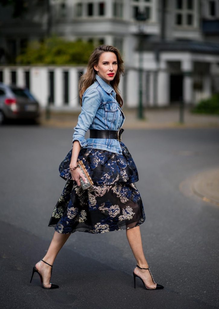 Alexandra Lapp wearing a Marchesa Notte dress with tiered corded lace and brocade in a mix of black, midnight-blue and gold by Marchesa Notte, blue trucker denim jacket by Levis, a gold buckle belt by Dorothee Schumacher, black Nosy t-bar Christian Louboutin sandals with a studded strap, handmade bracelet with rosegold fleur de lis lock by Coerlys and a vintage Chanel clutch in gold on May 3, 2018 in Duesseldorf, Germany.
