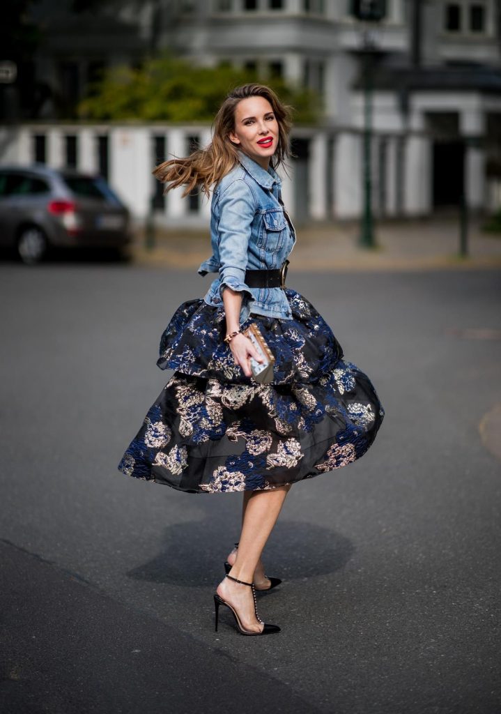 Alexandra Lapp wearing a Marchesa Notte dress with tiered corded lace and brocade in a mix of black, midnight-blue and gold by Marchesa Notte, blue trucker denim jacket by Levis, a gold buckle belt by Dorothee Schumacher, black Nosy t-bar Christian Louboutin sandals with a studded strap, handmade bracelet with rosegold fleur de lis lock by Coerlys and a vintage Chanel clutch in gold on May 3, 2018 in Duesseldorf, Germany.