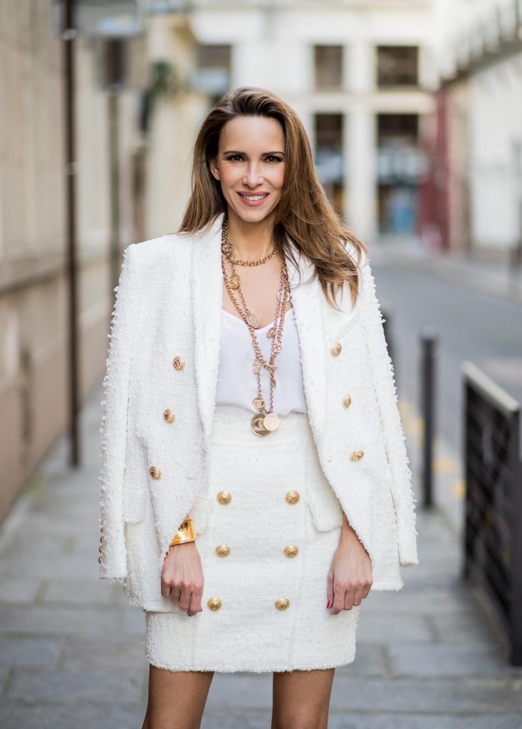 Alexandra Lapp in a full Balmain costume - a white tweed blazer with golden buttons and a matching tweed mini skirt with golden buttons both Balmain, a white silk top from Jadicted, heels from Christian Louboutin and Vintage necklaces from Chanel during Paris Fashion Week Womenswear Fall/Winter 2018/2019 on March 4, 2018 in Paris, France.