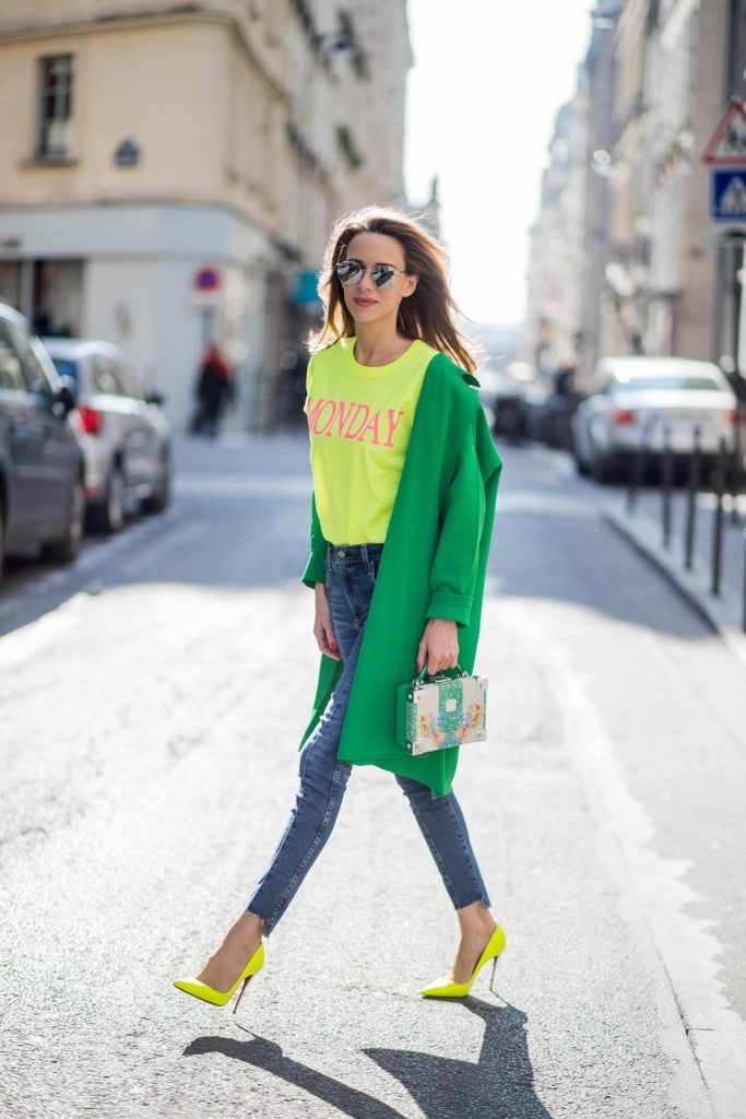 Alexandra Lapp in Mondays Statement Shirt Look wearing a yellow neon t-shirt with pink letters writing Monday by Alberta Ferretti, a blue pair of AG Jeans, a green coat from Stella McCartney, yellow neon pumps by Christian Louboutin, the Berlin cross body bag with crystal flowers from MCM and sunglasses by Le Specs during Paris Fashion Week Womenswear Fall/Winter 2018/2019 on March 5, 2018 in Paris, France.