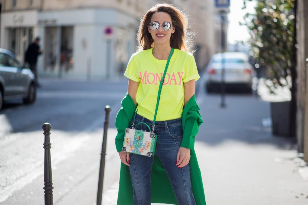 Alexandra Lapp in Mondays Statement Shirt Look wearing a yellow neon t-shirt with pink letters writing Monday by Alberta Ferretti, a blue pair of AG Jeans, a green coat from Stella McCartney, yellow neon pumps by Christian Louboutin, the Berlin cross body bag with crystal flowers from MCM and sunglasses by Le Specs during Paris Fashion Week Womenswear Fall/Winter 2018/2019 on March 5, 2018 in Paris, France.