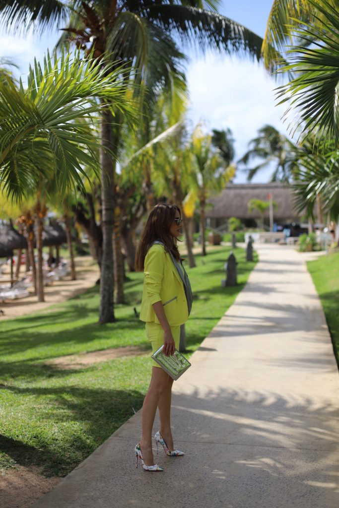 Alexandra Lapp in Yellow Mania wearing a yellow shift dress with zipper & a yellow como-blazer with hood, So Kate Loubitag red sole pumps with scribbled drawings, Louis Vuitton Monogram Miroir Pochette Plat Pouch and mirrored silver Aviator Le Specs seen on Mauritius during a press tour in April 2018.