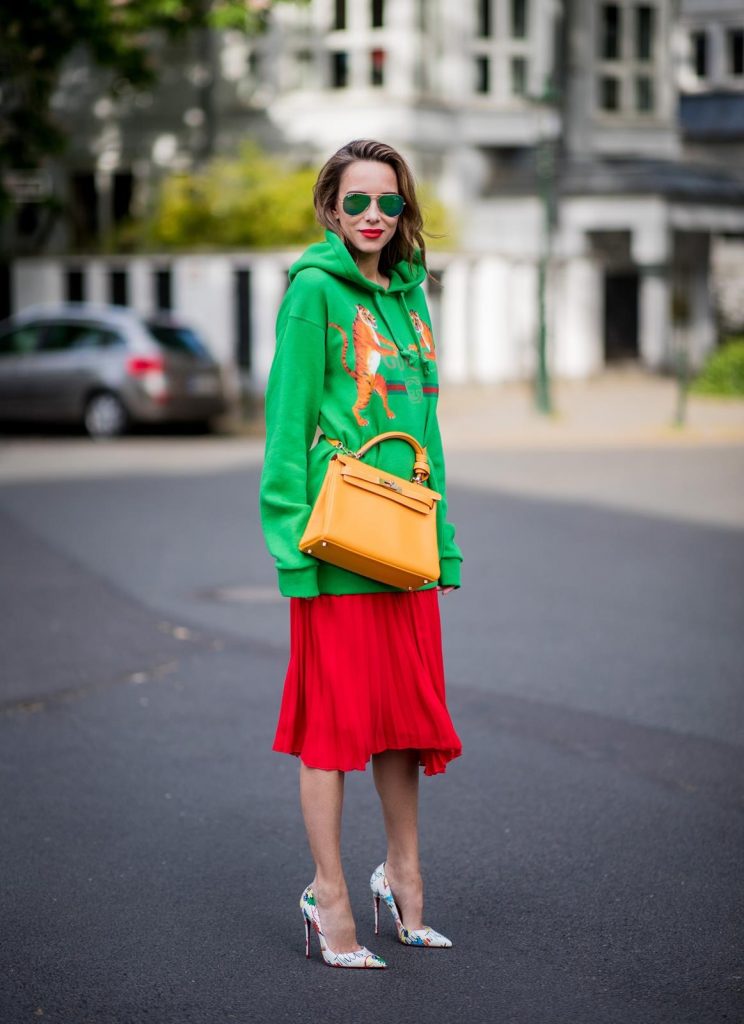 Gucci, SET, Hermès, Christian Louboutin, Ray Ban Alexandra Lapp in a Hermès Kelly Look wearing a green tiger print Gucci logo hoodie, a red pleated skirt by SET, a Hermes Birkin 30 bag in orange, Pigalle Follies pumps by Christian Louboutin and green mirrored Ray Ban sunglasses on May 3, 2018 in Duesseldorf, Germany.